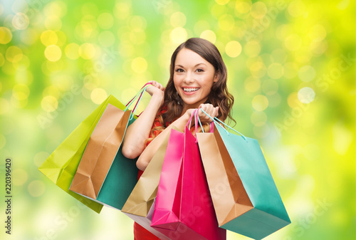 people and sale concept - young smiling woman with shopping bags over green background and lights