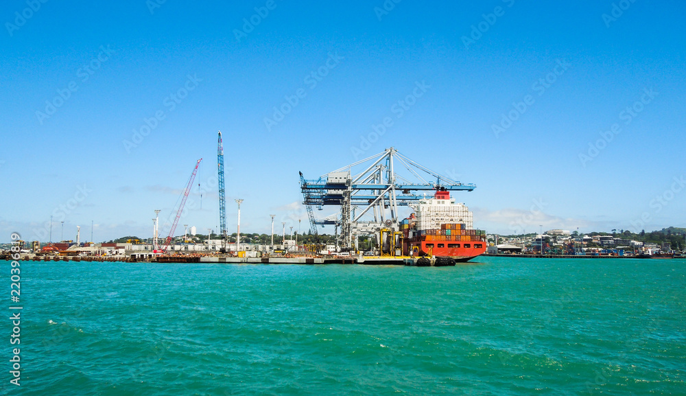 Large Cargo ship loading containers at the shipping dock in Auckland, New Zealand. Taken from a boat on the water on a sunny day.