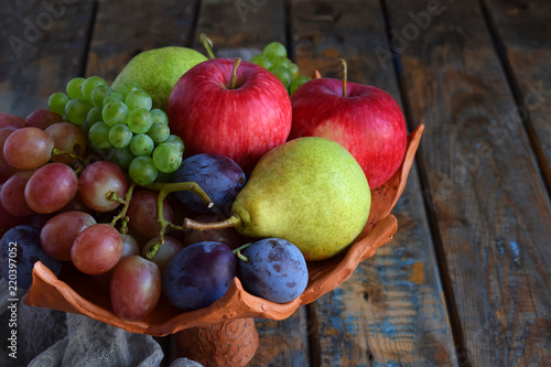 Autumn still life for thanksgiving with autumn fruits and berries on wooden background - grapes, apples, plums, viburnum, dogwood. Raw food. Copy space