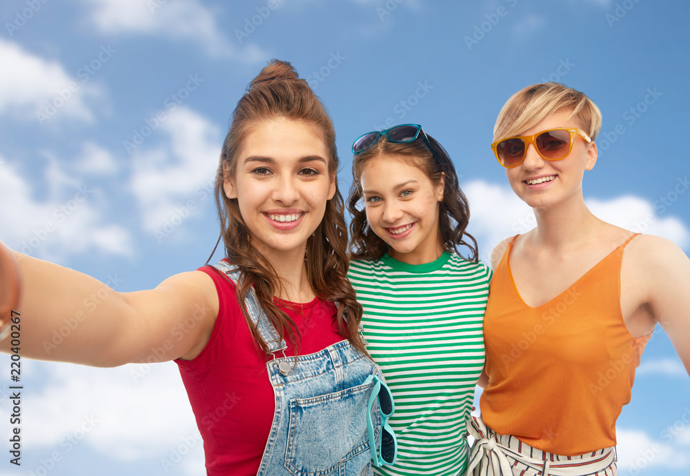 friendship and people concept - group of happy female smiling friends in sunglasses taking selfie over blue sky and clouds background friendship and people concept - group of happy female smiling friends in sunglasses taking selfie over blue sky and clouds background