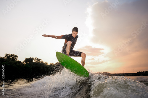 Young attractive man riding on the wakeboard on the background of evening sky