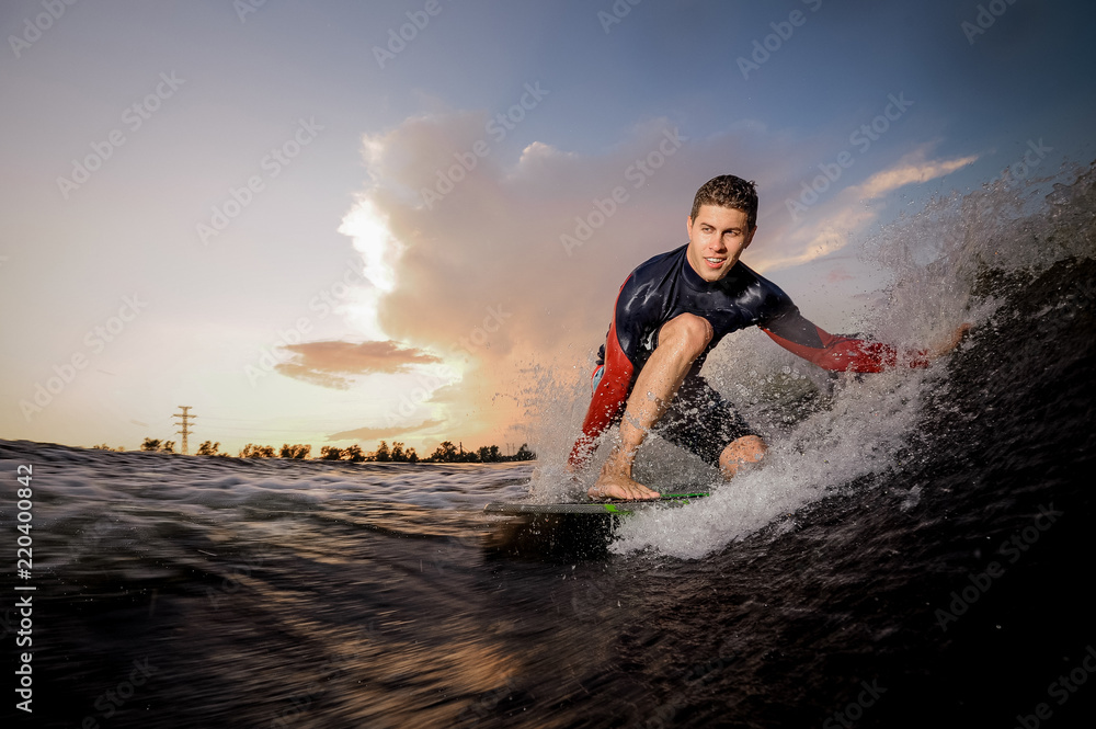Active young male wakeboarder riding on the one knee on the board