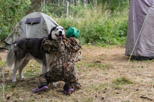 Girl is hugging a happy husky dog. Back view. Camping with tourist tents in the forest.