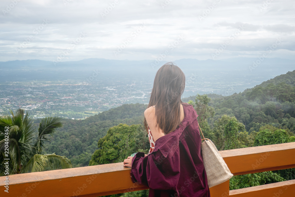 The Asian woman is looking to the city and mountain view from the balcony in Thailand. 