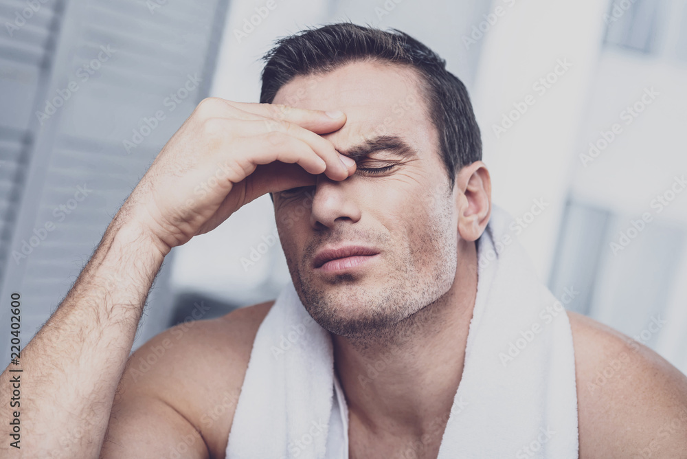 Fatigue. Tired thoughtful man having unhealthy appearance while compressing the bridge of the nose with the fingers while keeping his eyes closed Fatigue. Tired thoughtful man having unhealthy appearance while compressing the bridge of the nose with the fingers while keeping his eyes closed