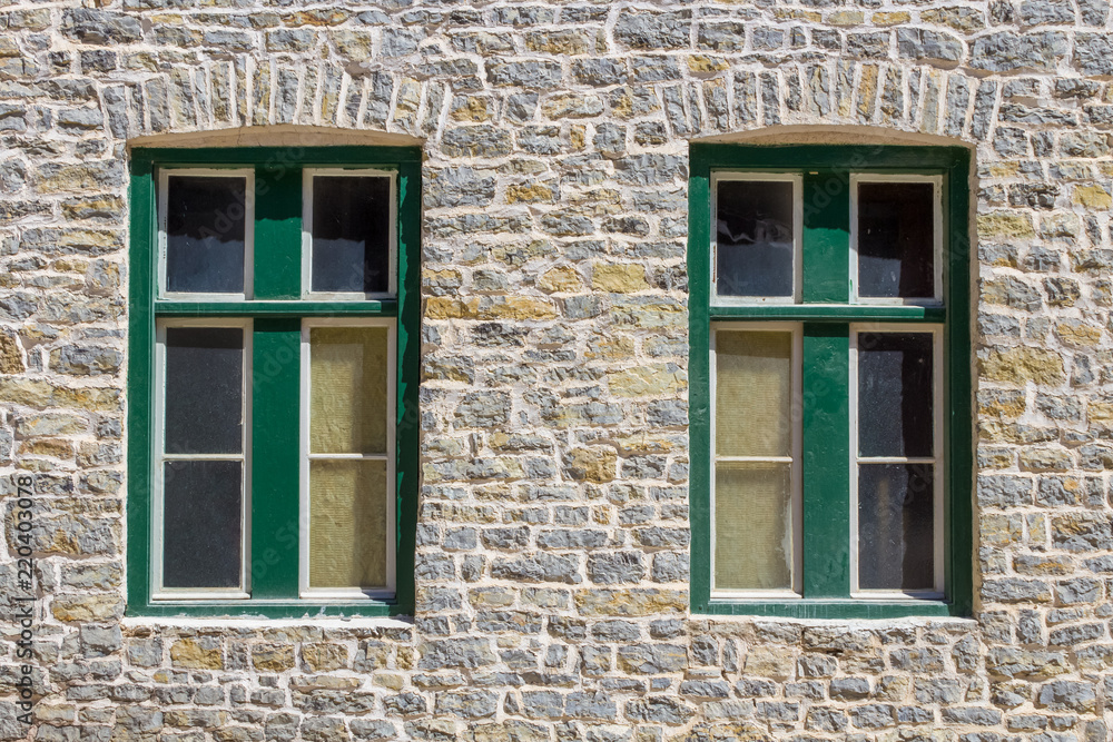 Two green windows in a stone brick wall of an old house