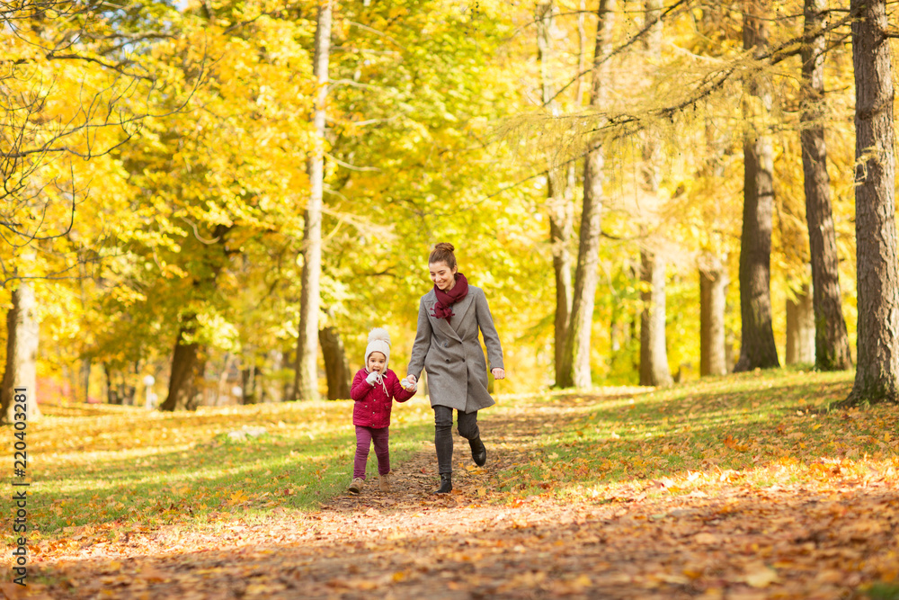family, season and people concept - happy mother and little daughter walking along autumn park