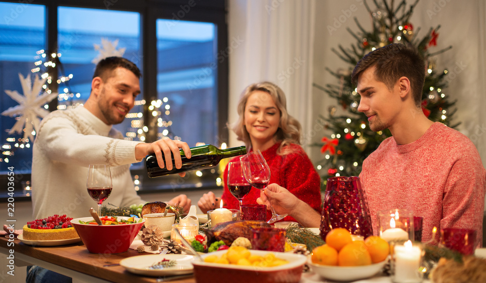 holidays and celebration concept - happy friends having christmas dinner at home and drinking red wine holidays and celebration concept - happy friends having christmas dinner at home and drinking red wine