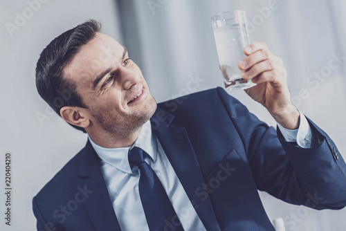 Have a drink. Cheerful handsome man holding a water glass while going to drink