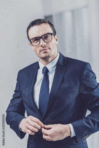 Confidence in himself. Portrait of a handsome presentable man in business clothes and glasses buttoning his jacket while looking at camera photo