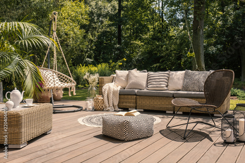 A rattan patio set including a sofa, a table and a chair on a wooden deck in the sunny garden. photo