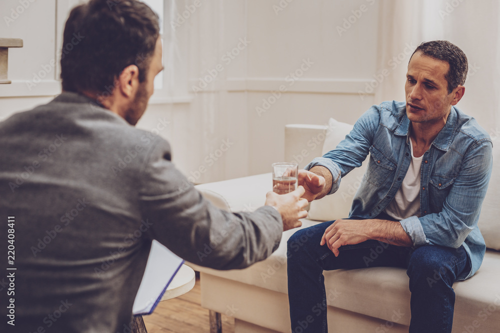 Obraz premium Keep calm. Upset patient sitting in cabinet opposite his practitioner and going to drink water