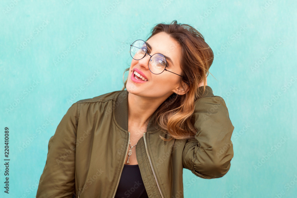 fashion girl in round glasses stands posing near a turquoise wall fashion girl in round glasses stands posing near a turquoise wall
