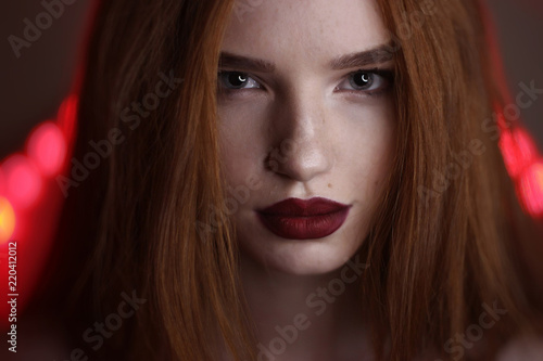 Young redhead lady with freckless over red lighting background.