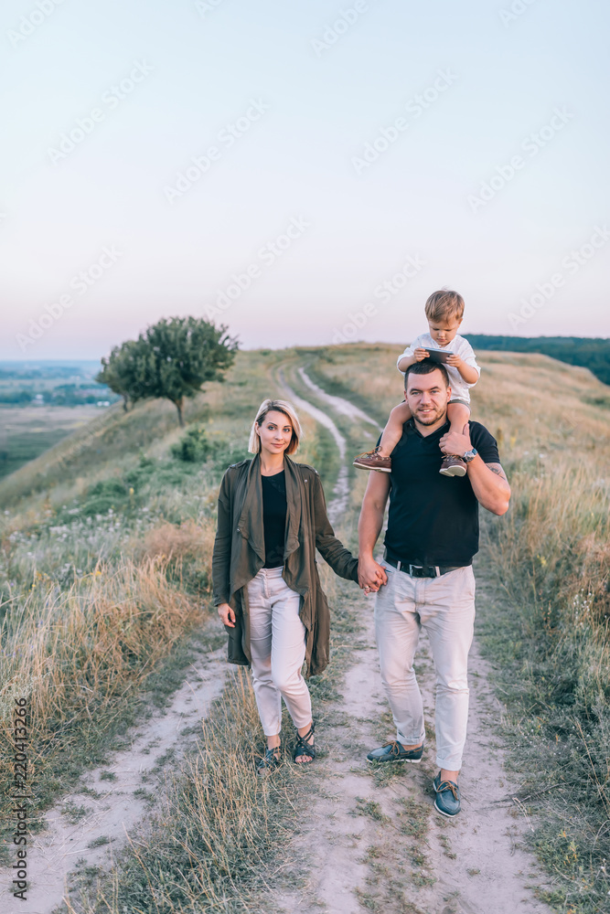beautiful happy young family with one child walking together and looking at camera in rural landscape