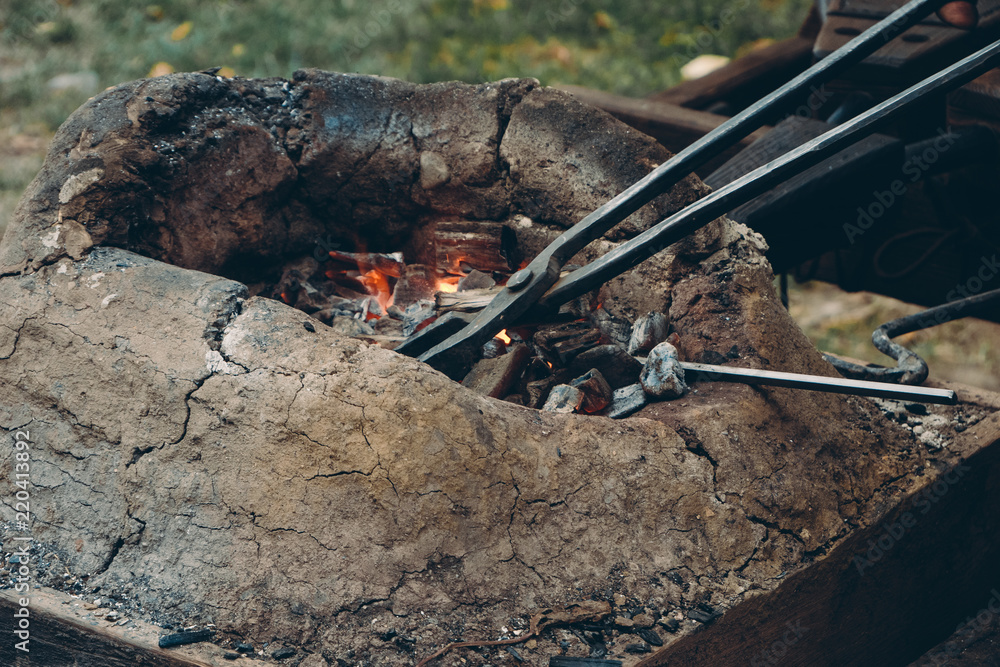 Fototapeta premium Close up of medieval furnace with iron tongs, burning coals and fire in blacksmith forge