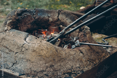 Close up of medieval furnace with iron tongs, burning coals and fire in blacksmith forge