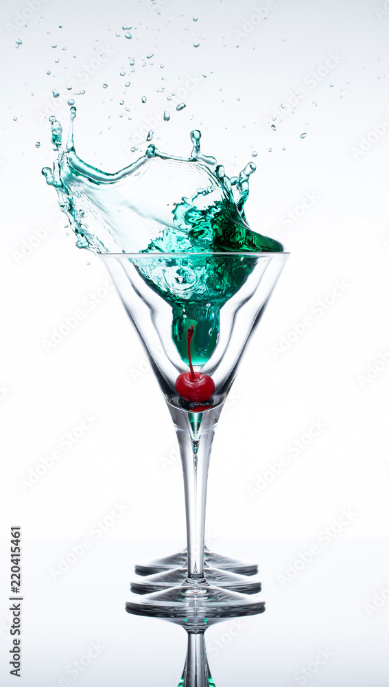 Red cherry dropped into a martini glass filled with a green drink creating a splash