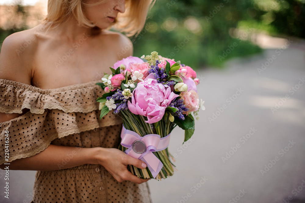 Blonde woman in beige dress holding a tender pink bouquet of flowers
