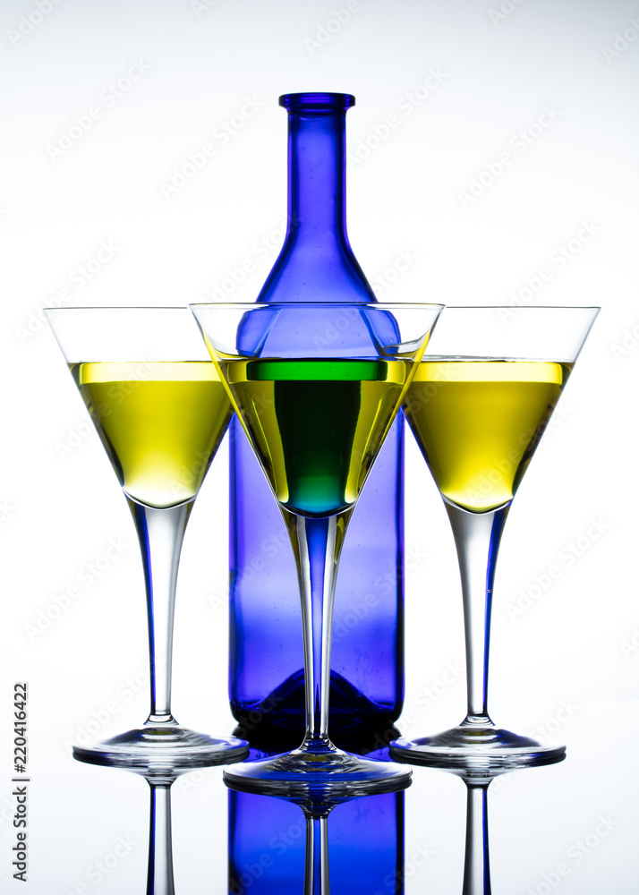 Three martini glasses in front of a blue bottle against a white background. Glasses filled with a yellow drink Three martini glasses in front of a blue bottle against a white background. Glasses filled with a yellow drink