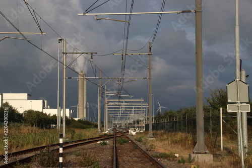 Dark clouds above railroad track with a switch in the port of Amsterdam with chimney with steam in background. photo