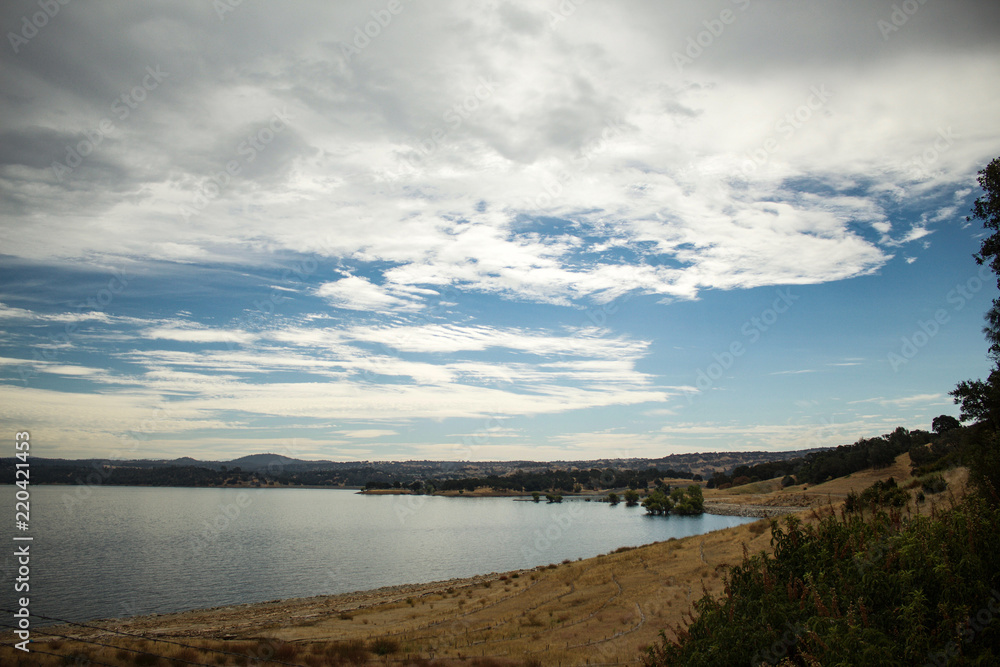 Folsom lake on a partly cloudy day during summer. Brown grass on shore, still lake water