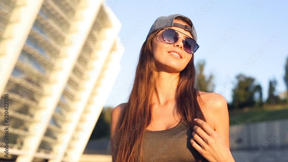 Poprttrait of happy, smiling young woman. Standing at the street in the sunglasses and holding longboard. Poprttrait of happy, smiling young woman. Standing at the street in the sunglasses and holding longboard.