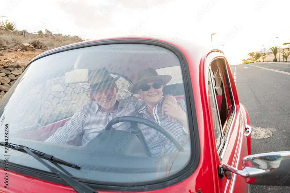 nice adult couple hug and love inside a red old vintage car parked on the road. smiles and have fun traveling together. happiness and lifestyle for nice people. summer time and vacation journey
