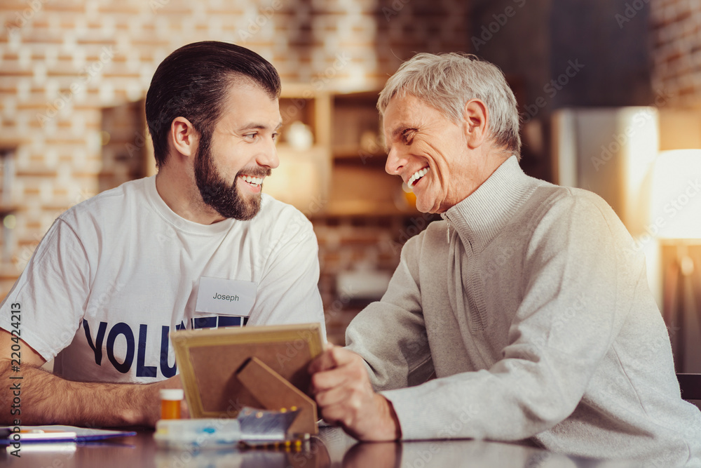 Funny story. Happy pleasant friendly men spending time together in the comfortable room smiling and overlooking a photo. Funny story. Happy pleasant friendly men spending time together in the comfortable room smiling and overlooking a photo.