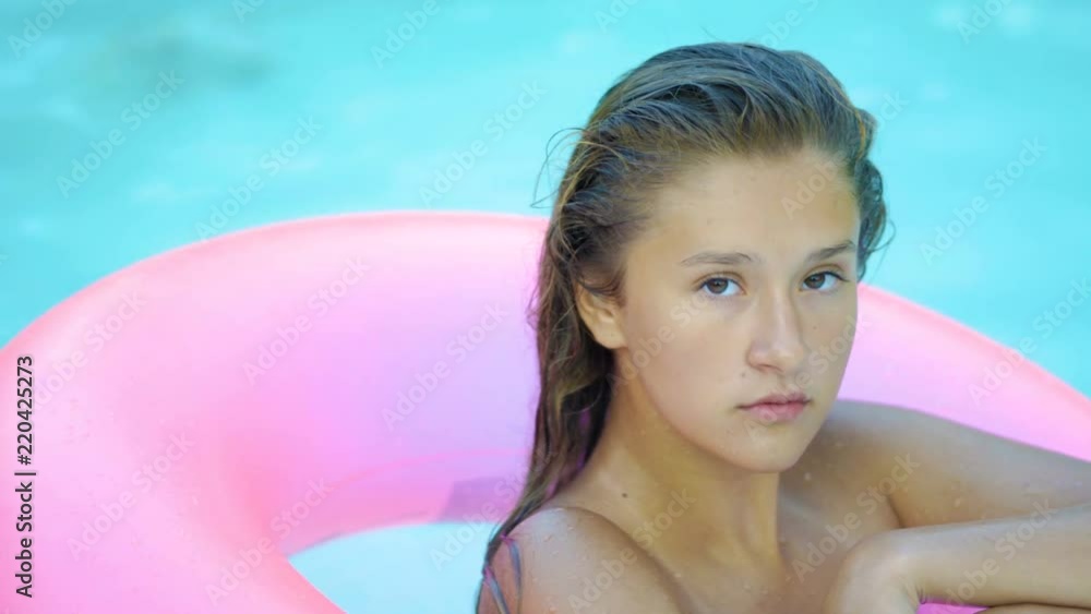 Happy girl relaxing on inflatable pink doughnut float. Young woman in bikini enjoying summer vacation drinking cocktails on pink floatie in pool Happy girl relaxing on inflatable pink doughnut float. Young woman in bikini enjoying summer vacation drinking cocktails on pink floatie in pool