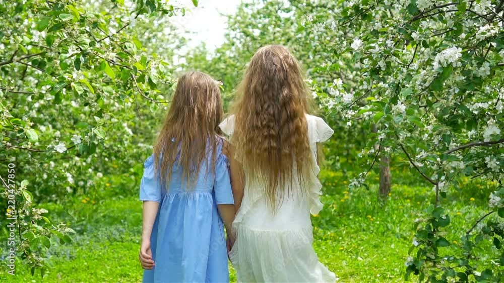 Adorable little girls in blooming apple tree garden on spring day Adorable little girls in blooming apple tree garden on spring day