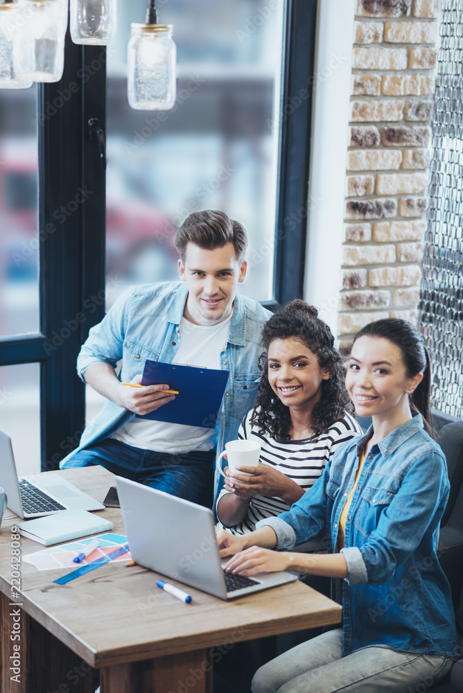 Huge revenue. Jovial three colleagues working at cafe while staring at camera Huge revenue. Jovial three colleagues working at cafe while staring at camera