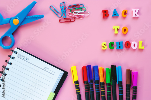 School supplies with opened notebook, coloured pen, scissors, binder clip and wooden text BACK TO SCHOOL on pink background for education concept