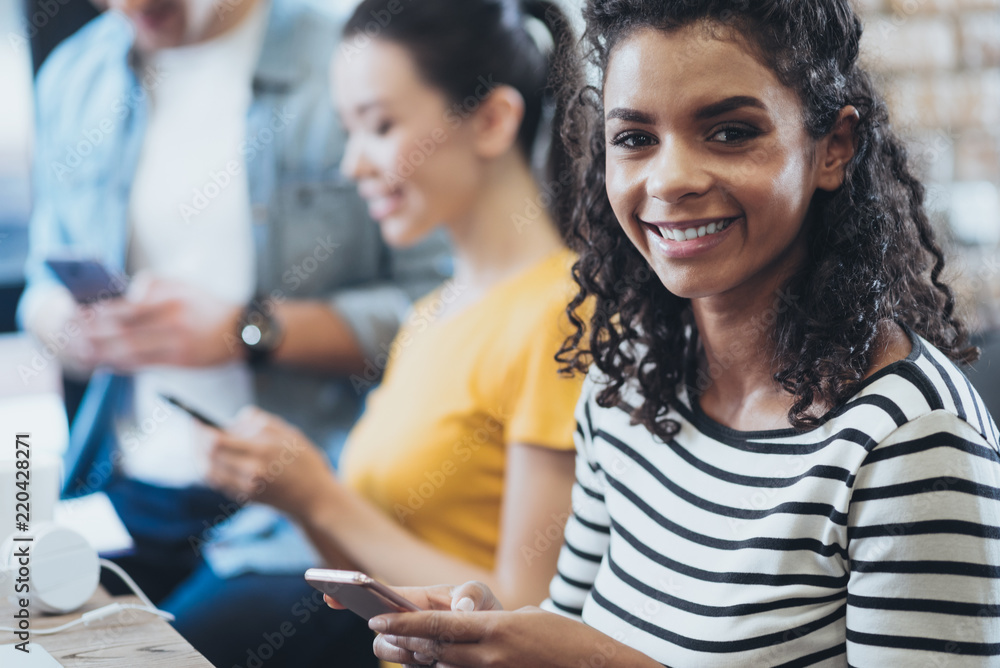 No live communication. Three friends using smartphones while cheerful beautiful woman grinning to camera No live communication. Three friends using smartphones while cheerful beautiful woman grinning to camera
