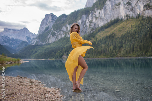 Beautiful girl in a light yellow dress by the lake in the mountains  