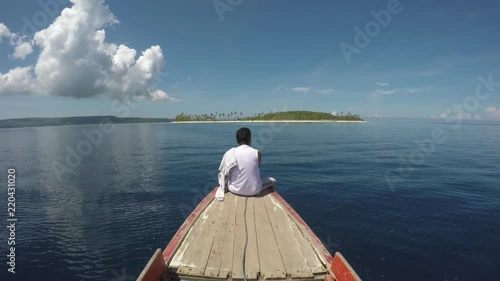 Happy man sitting on small boat going to tropical white sand uninhabitat island photo