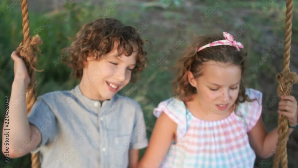 Brother and sister are having fun riding on the swings. Dynamic video. holidays in the countryside