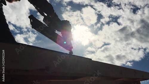 Construction worker using a nail gun on a roof with a blue sky in the background.