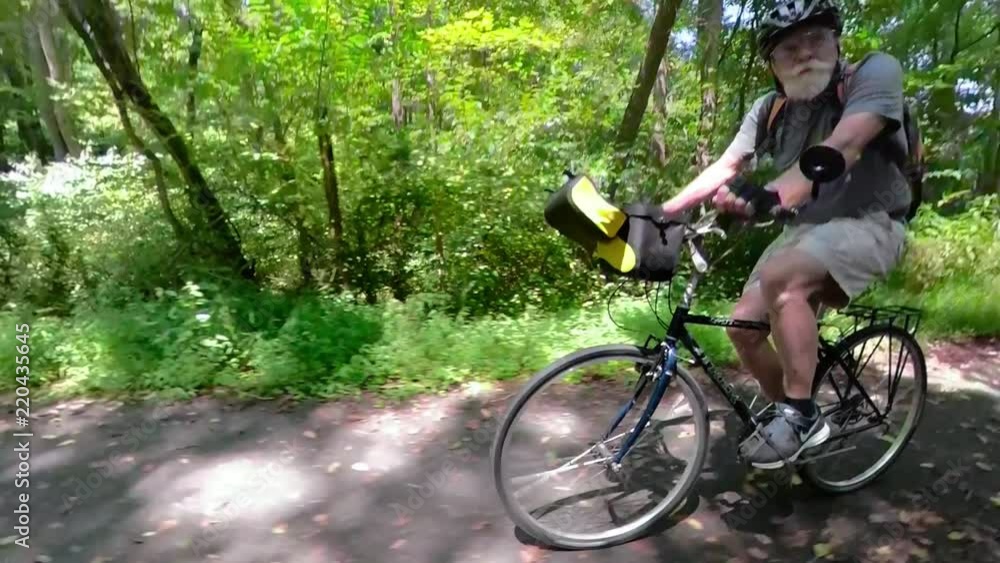 Camera pans as biker passes an elderly man biking on a paved trail