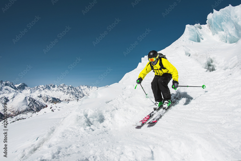 Professional skier at the speed before jumping from the glacier in winter against the blue sky and mountains