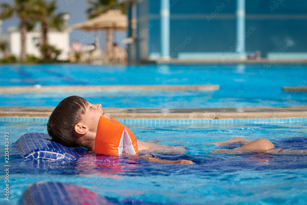 Portrait of happy Caucasian boy having fun in pool at resort. He is on water sunbed.