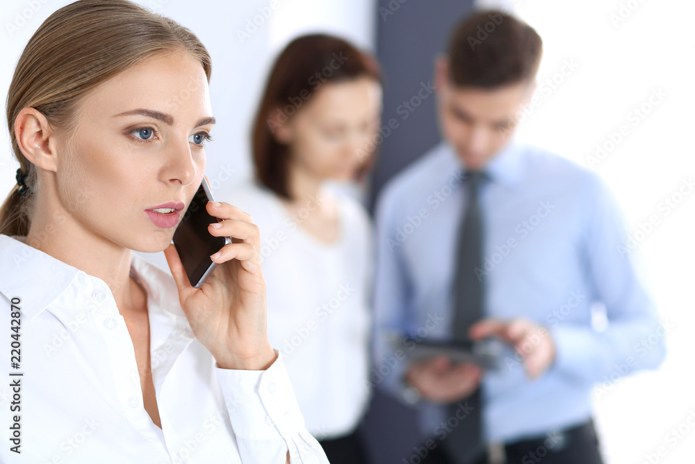 Serious blonde businesswoman talking by phone in the background of her colleagues in office. Business concept Serious blonde businesswoman talking by phone in the background of her colleagues in office. Business concept