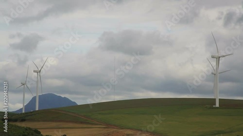 Wind turbines spinning in green hills with cloudy sky