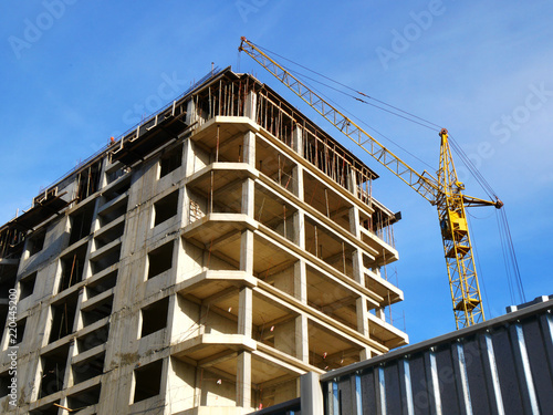 Industrial crane near building. Concrete building under construction. Construction site background.