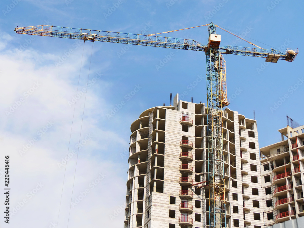 Huge crane near building. Concrete building under construction. Construction site.