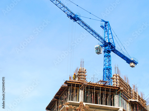Construction crane and concrete building against blue sky. Construction site.