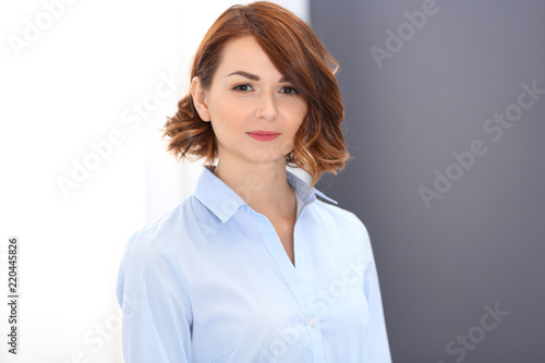 Young brunette business woman looks like a student girl working in office. Caucasian girl standing straight