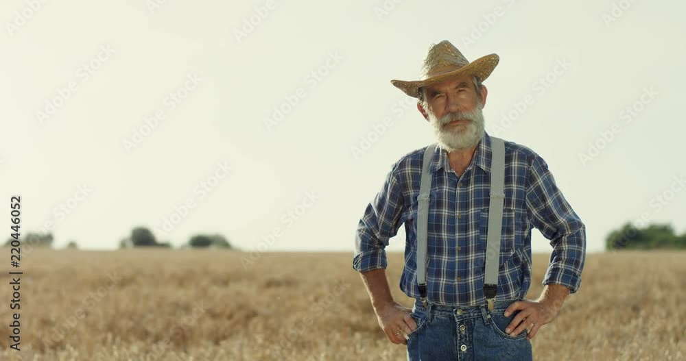 Portrait of the Caucasian grey haired old man in a hat looking at the side, then turning his head and smiling to the camera. At the wheat field. Portrait of the Caucasian grey haired old man in a hat looking at the side, then turning his head and smiling to the camera. At the wheat field.