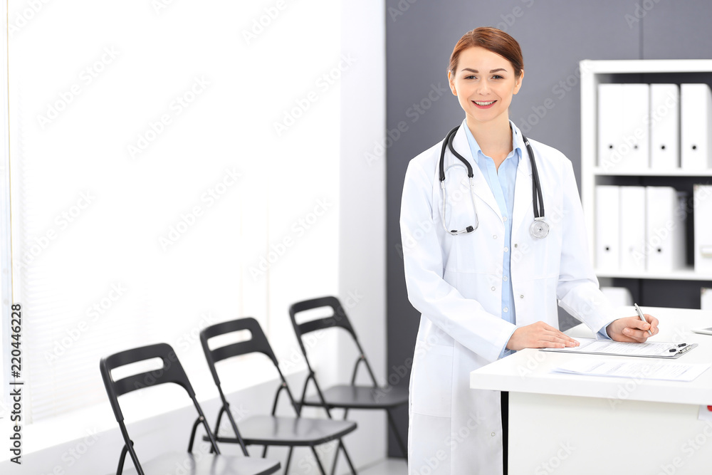 Doctor woman at work. Portrait of female physician filling up medical form while standing near reception desk at clinic or emergency hospital. Medicine concept Doctor woman at work. Portrait of female physician filling up medical form while standing near reception desk at clinic or emergency hospital. Medicine concept