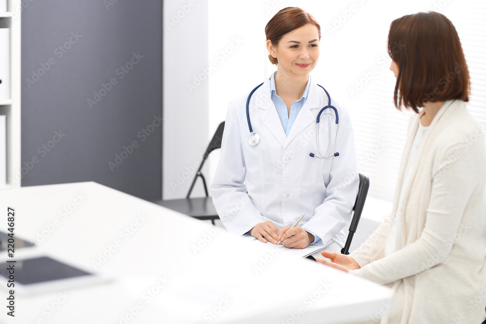 Happy doctor and patient discussing something while sitting at the chairs at hospital. Physician at work in clinic. Medicine and healthcare concept Happy doctor and patient discussing something while sitting at the chairs at hospital. Physician at work in clinic. Medicine and healthcare concept